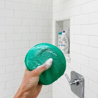 A Clean Logic round dual-texture exfoliating body scrubber, designed to gently scrub away dead skin cells and impurities. Features a soft side for gentle cleansing and a textured side for deeper exfoliation. Ideal for restoring skin's natural glow and leaving it smooth and refreshed.